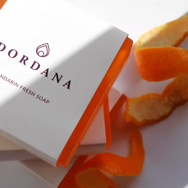 A summer shadow is cast on a single bar of Dordana's Mandarin Fresh soap and a spiral of mandarin peel
