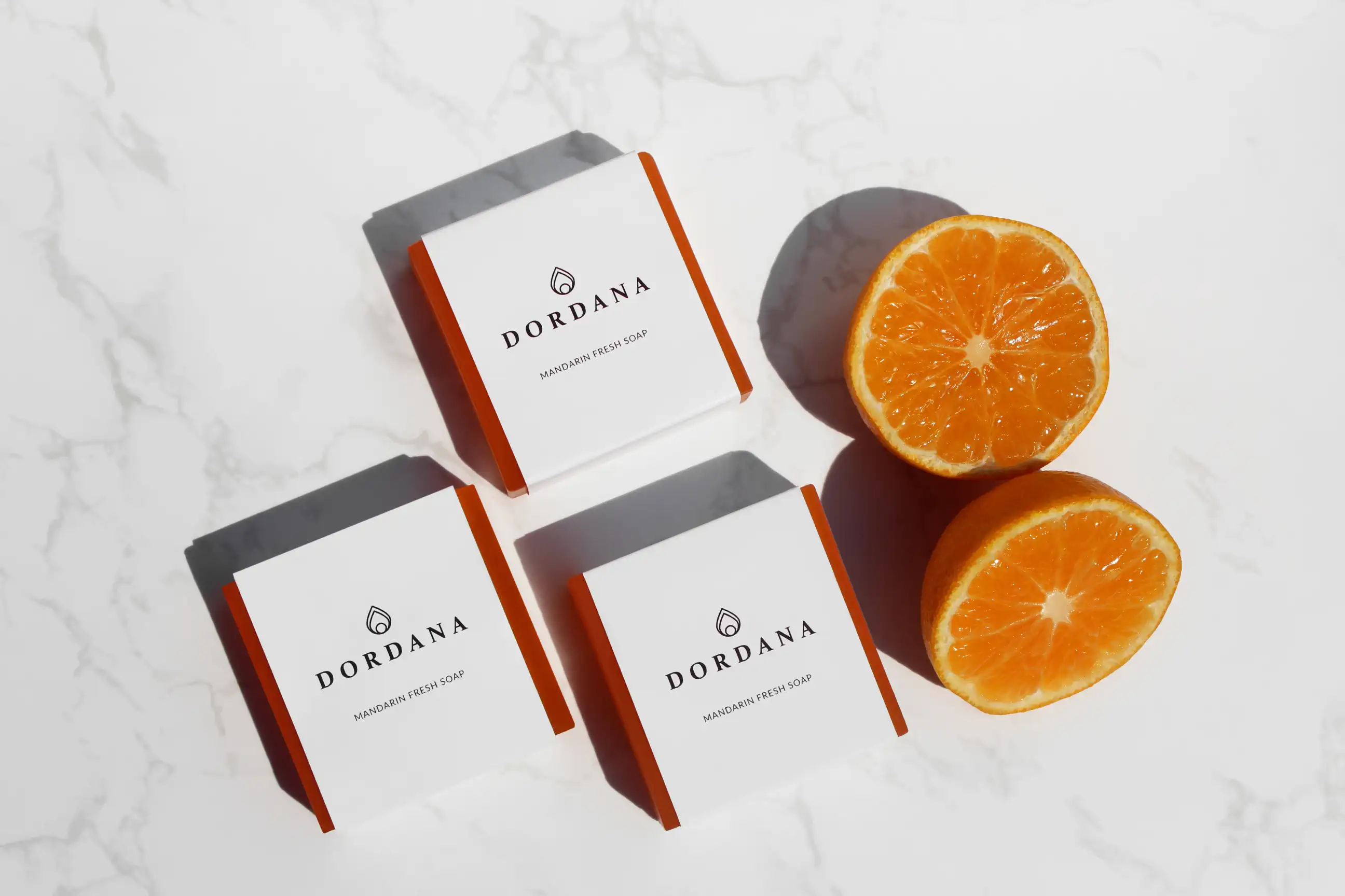 Wrapped bars of Dordana's Mandarin Fresh soap accompanied by succulent mandarins.