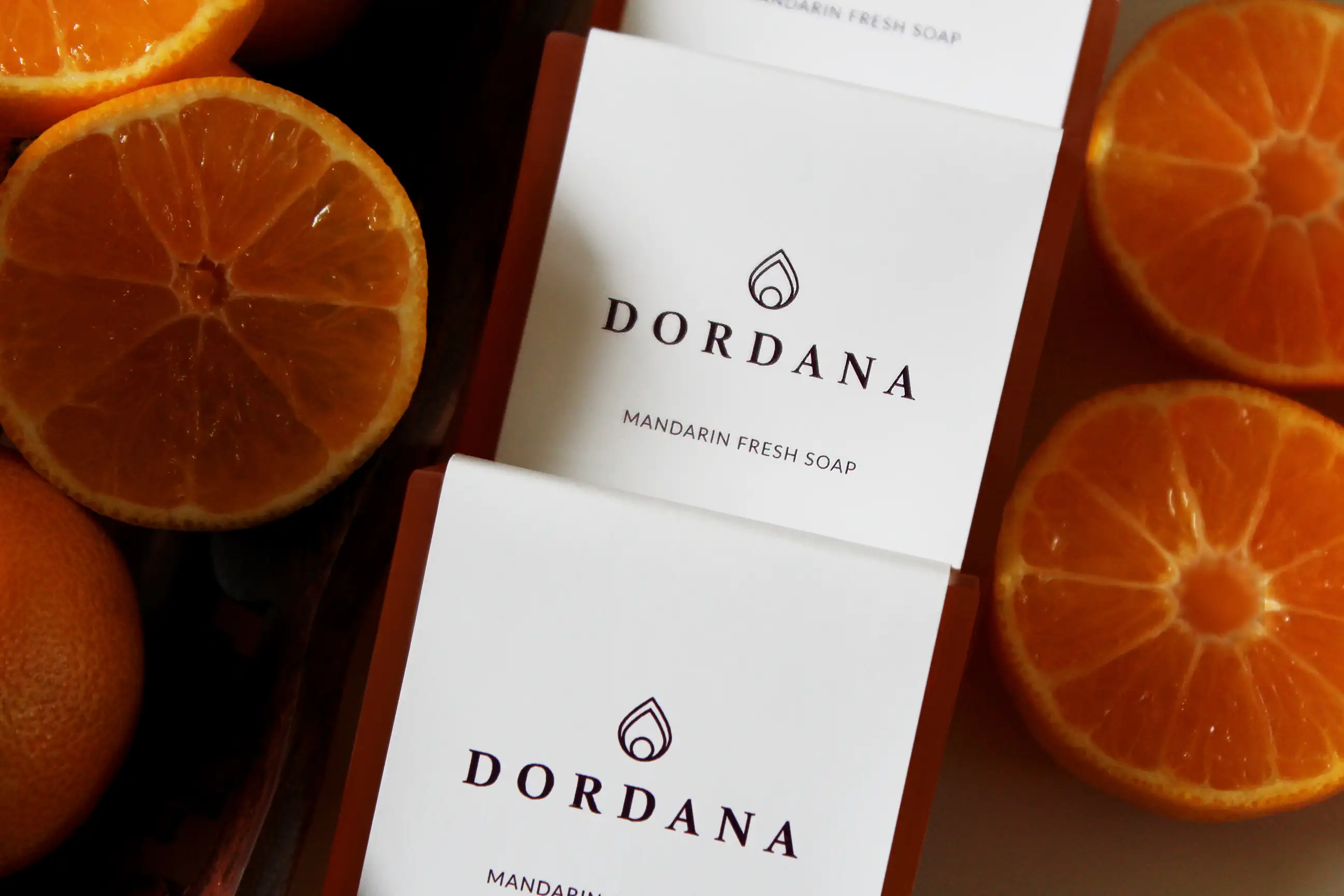 Wrapped bars of Dordana's Mandarin Fresh soap accompanied by succulent mandarins.