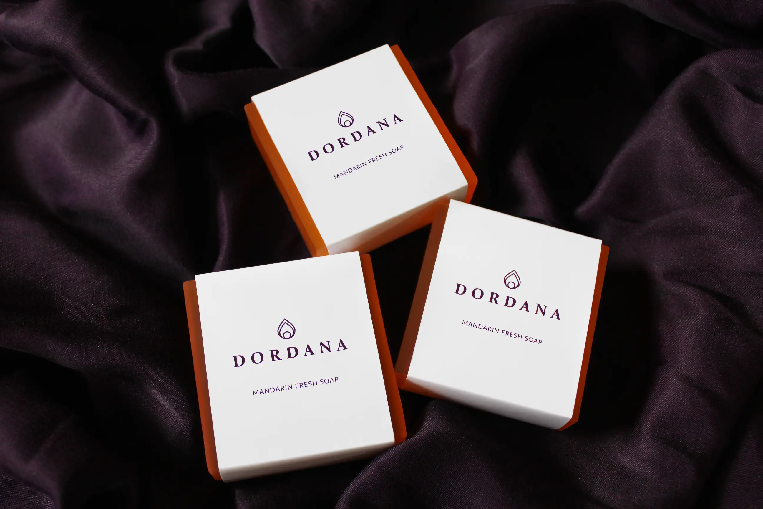 Wrapped bars of Dordana's Mandarin Fresh soap framed by undulating swirls of rich purple fabric.